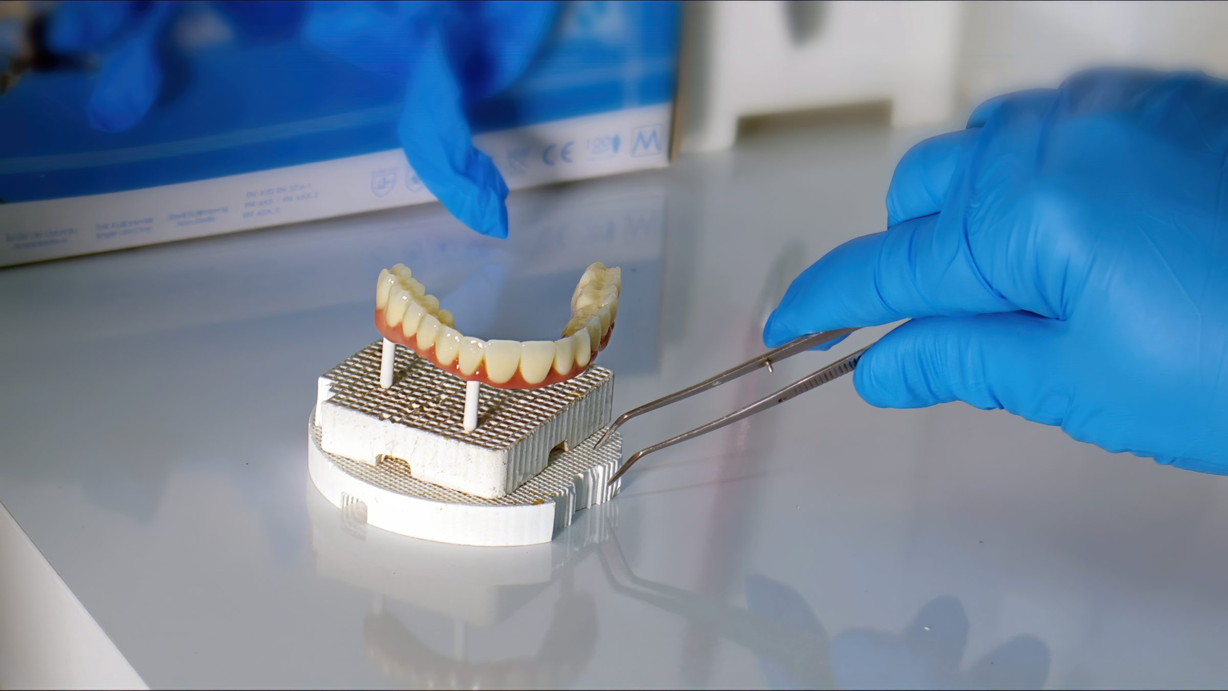 Gloved technician handling a finished full-arch dental prosthesis on a firing tray in a dental lab