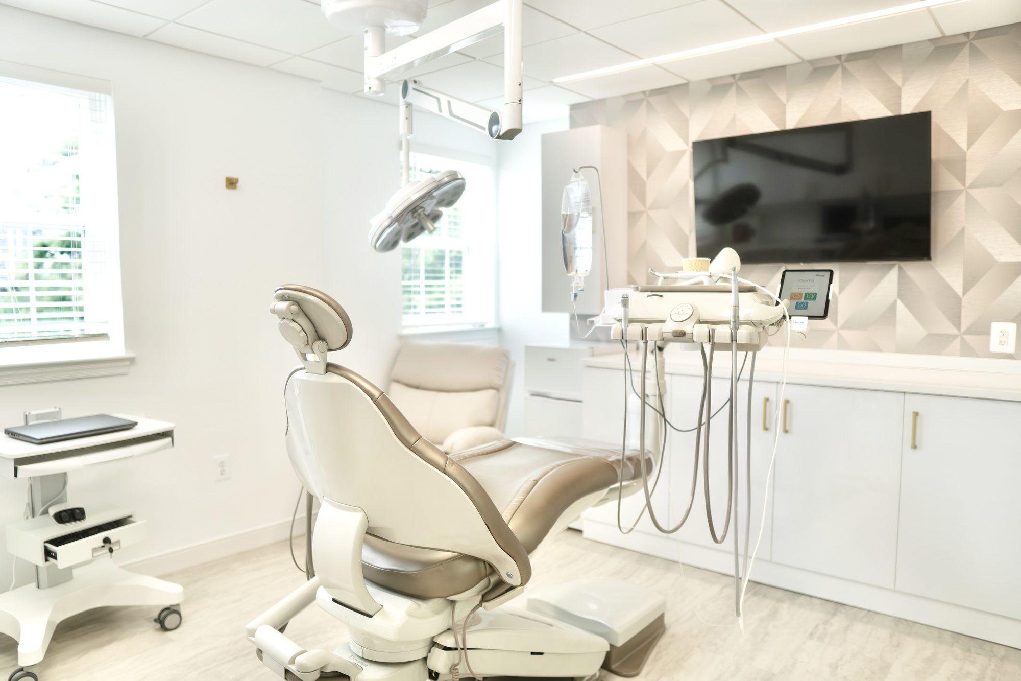 A treatment room at Dr. Nahlah's Alexandria office, with a cream dental chair and a wall-mounted screen