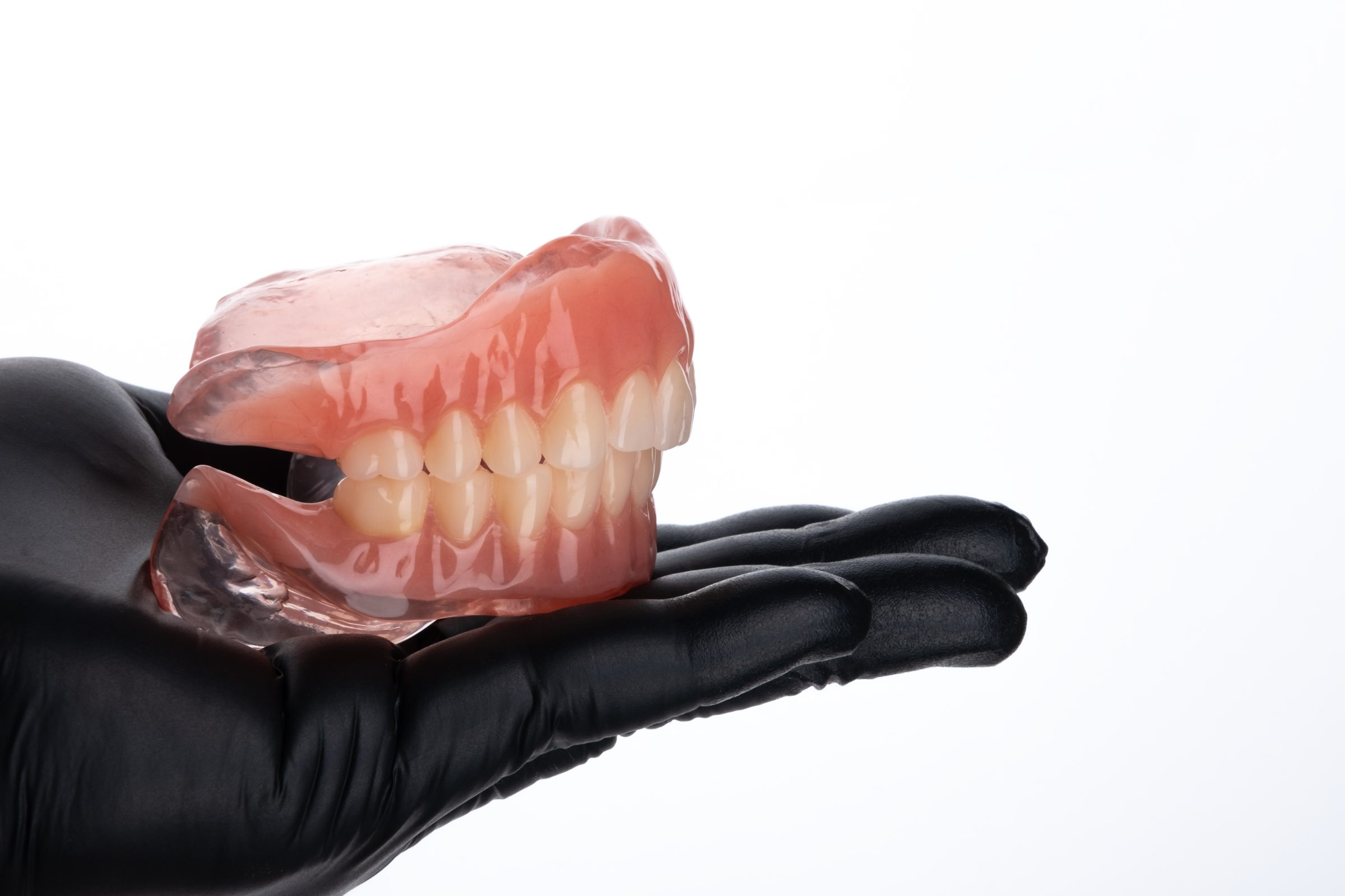 Gloved hand holding a full set of conventional removable upper and lower dentures