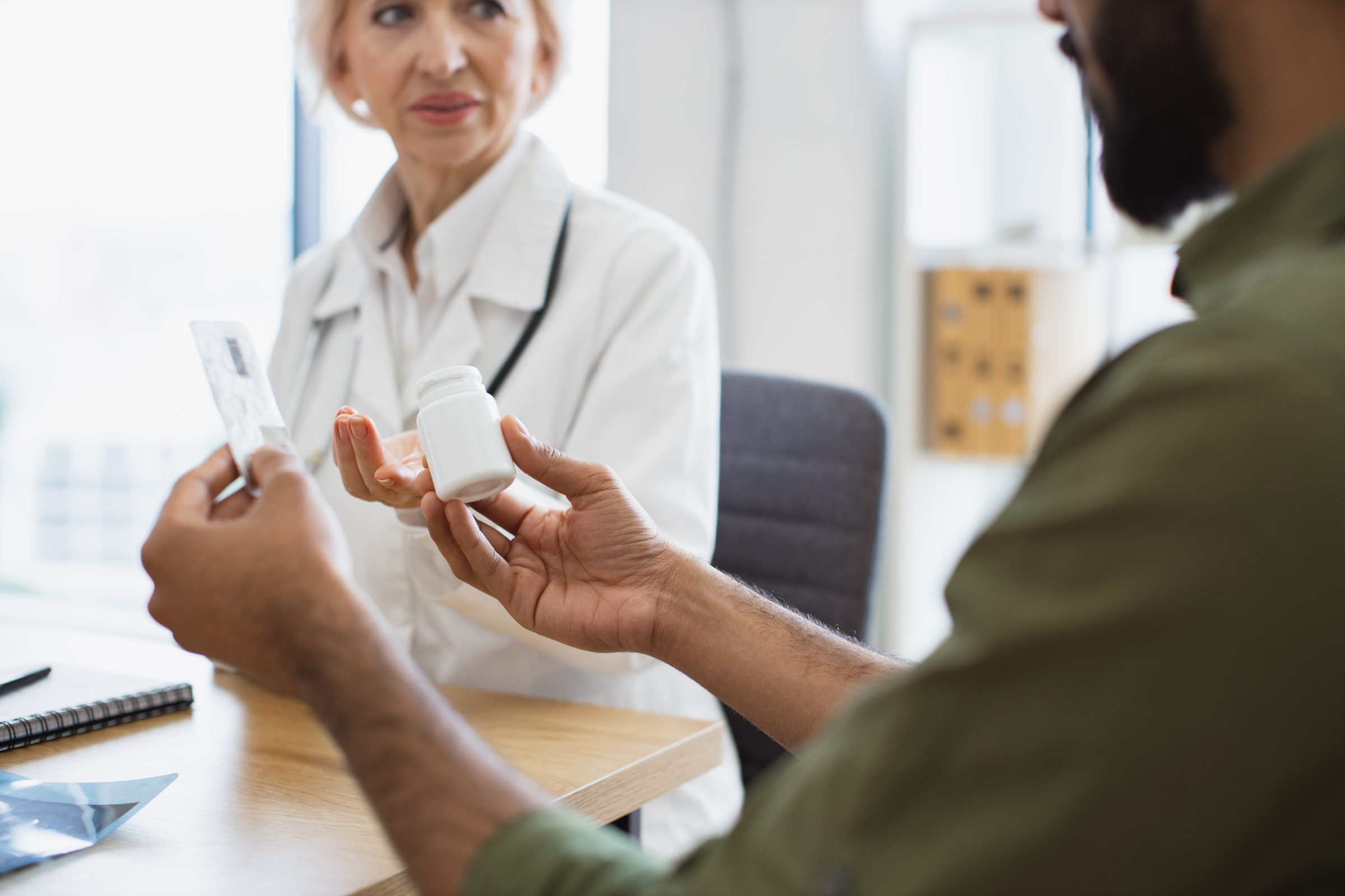 Patient holding a pill bottle while a doctor explains the medication across a desk
