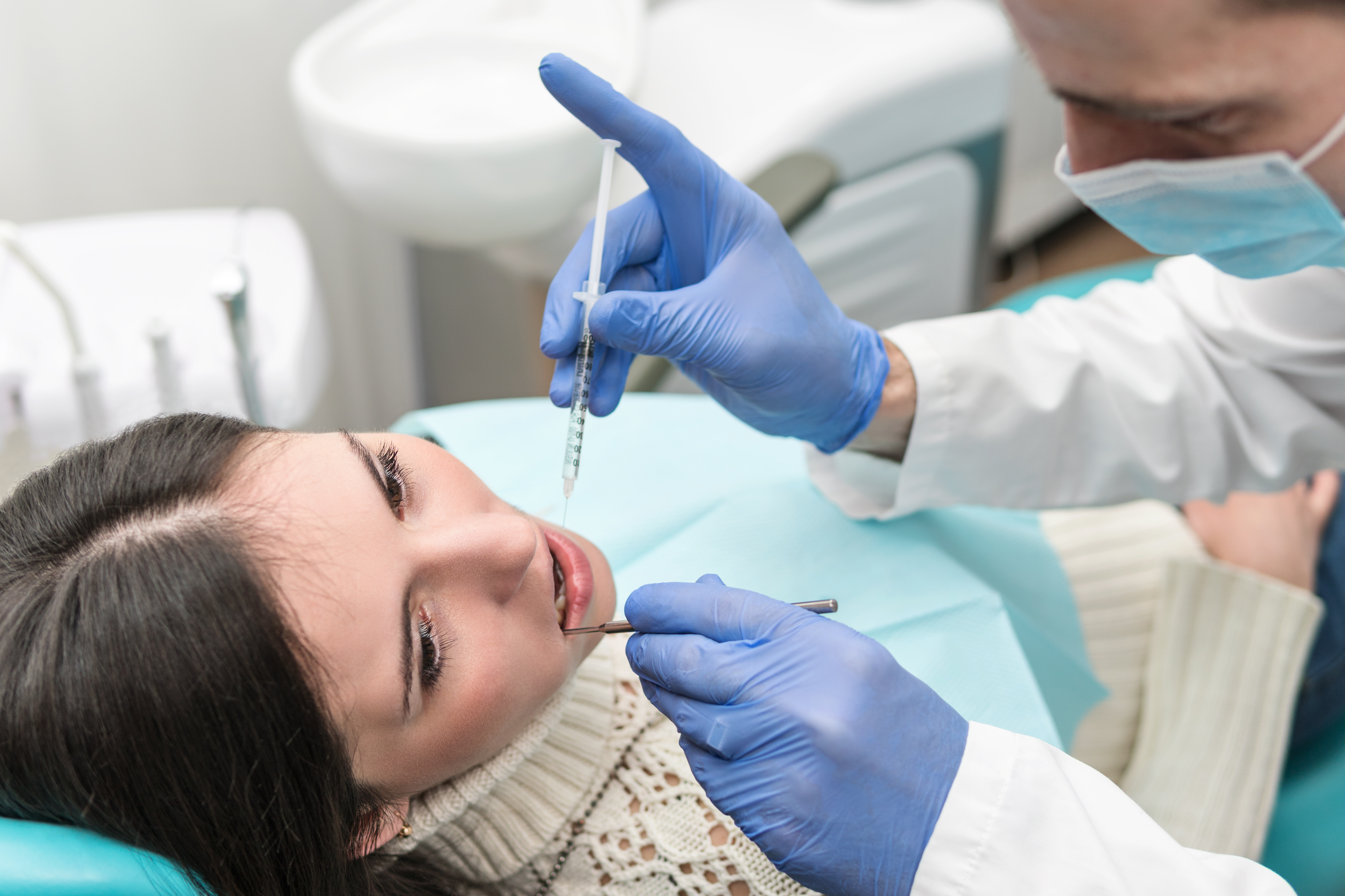 Dentist in gloves and a mask preparing a local anesthetic injection for a patient in the chair