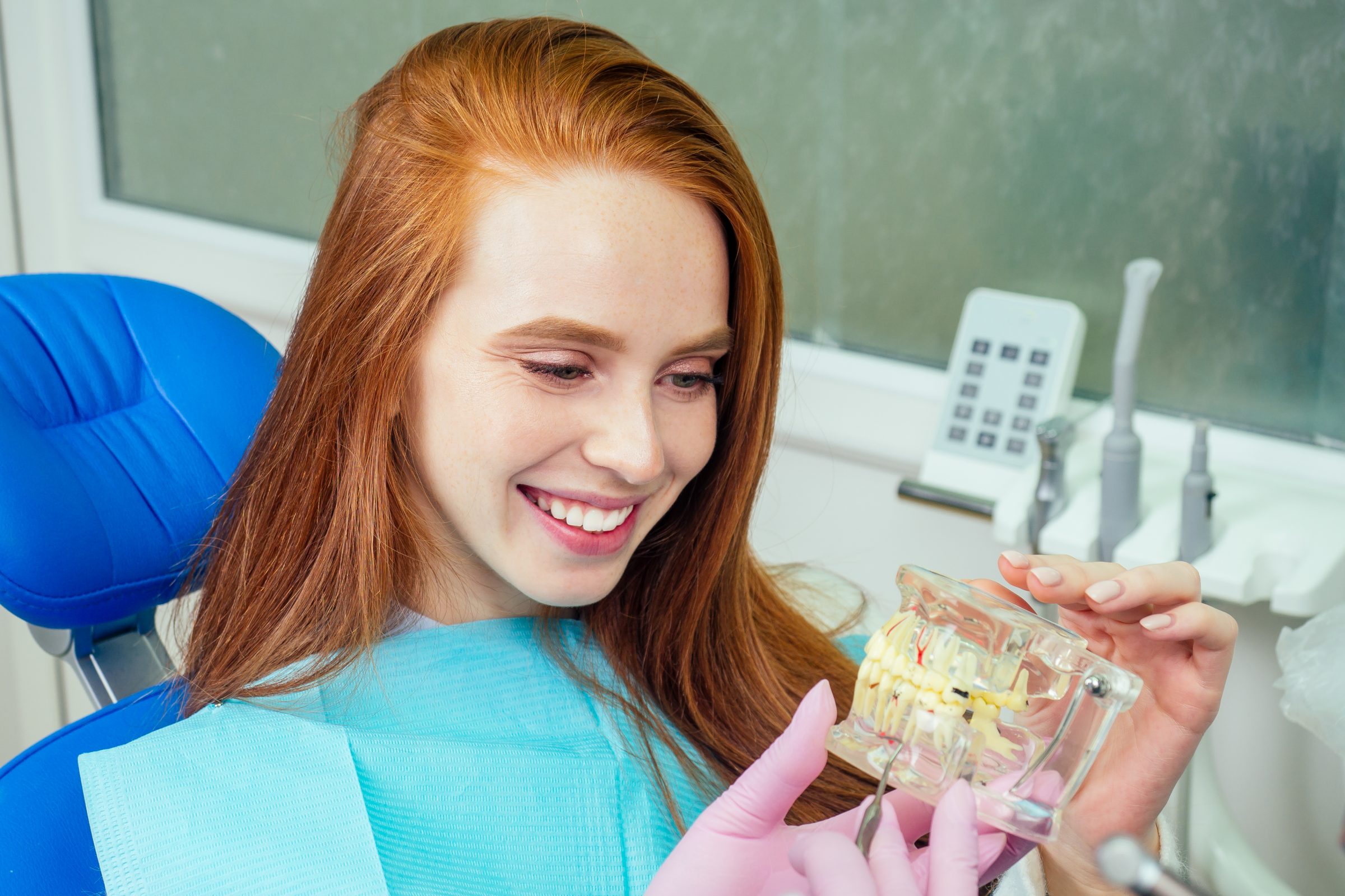 Smiling patient in the dental chair holding a model of the teeth